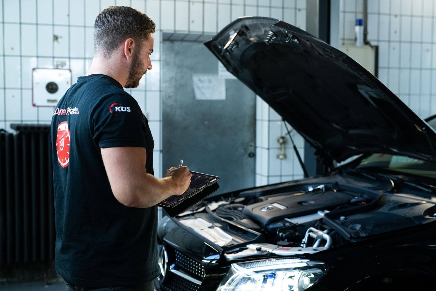 Mann bei der Inspektion eines Mercedes, die Motorhaube ist offen